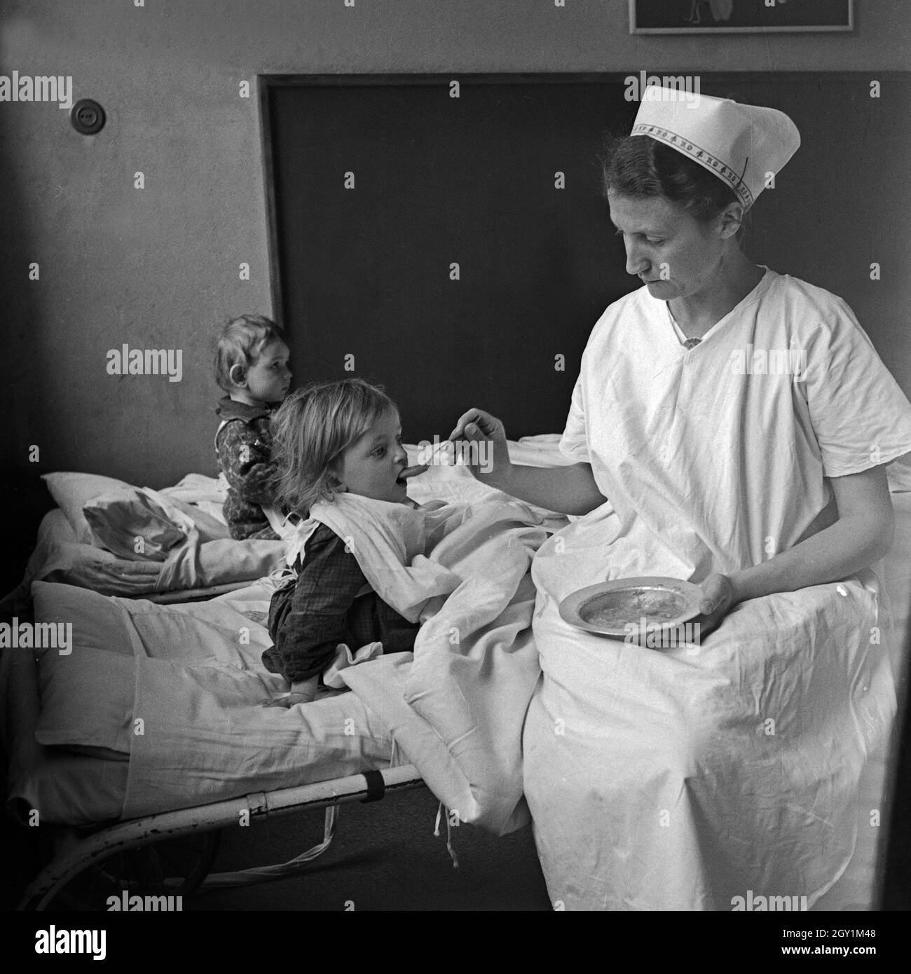Eine Krankenschwester füttert Kleinkinder im Mütterheim Dresden auf Schloß Dittersbach, Deutschland 1930er Jahre. A nurse feeding toddlers at the rest centre for mothers at Dittersbach castle near Dresden, Germany 1930s. Stock Photo