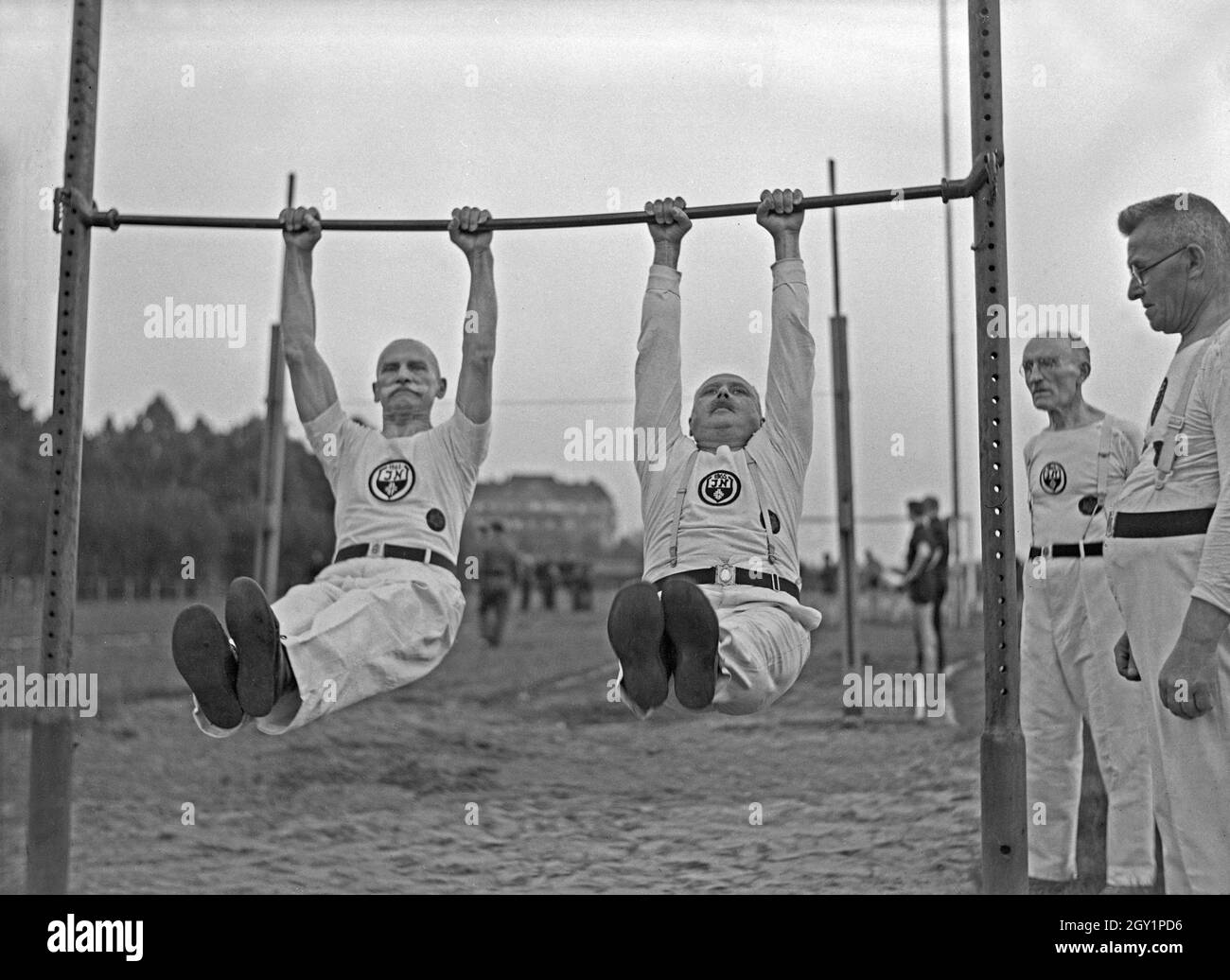 Zwei Turner aus der Altherrenriege eines Turnvereins tragen eine Übung am Reck vor, Deutschland 1930er Jahre. Two members of the senior department of a gymnastic club performing at a high bar on a sporting ground, Germany 1930s. Stock Photo