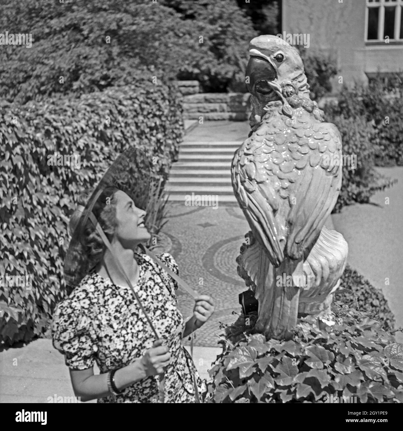 Eine junge Frau bei einer Papageienstatue in einem Park, Deutschland 1930er Jahre. A young woman and a sculpture of a parrot at a public garden, Germany 1930s. Stock Photo