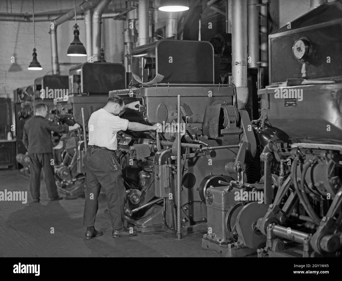 Arbeiter an ihren Maschinen in einer Fabrikhalle, Deutschland 1930er Jahre. Workers with their machines in a factory hall, Germany 1930s. Stock Photo