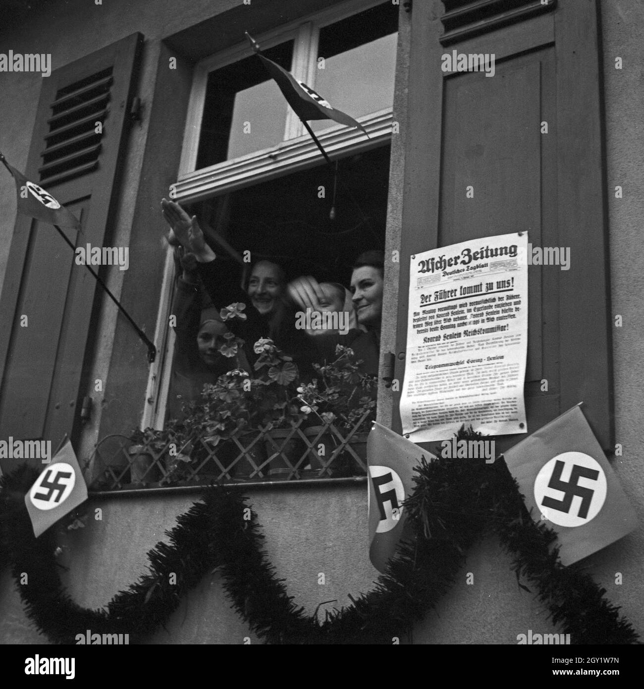 Menschen in den Fenstern bejubeln Führer und Reichskanzler Adolf Hitler bei seinem Besuch in Asch im Sudetenland, Deutschland 1930er Jahre. People cheering to Fuehrer and chancellor Adolf Hitler out of their windows visiting the city of Asch in Sudetenland county, Germany 1930s. Stock Photo