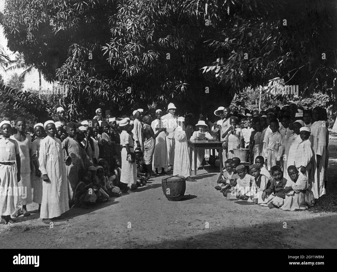 Frauen der Deutsch Ostafrikanischen Gesellschaft verteilen Chinin an afrikanische Schulkinder, Deutsch-Ostafrika 1900er Jahre. Women of the German East African Society giving quinine to African school kids, German East Africa 1900s. Stock Photo