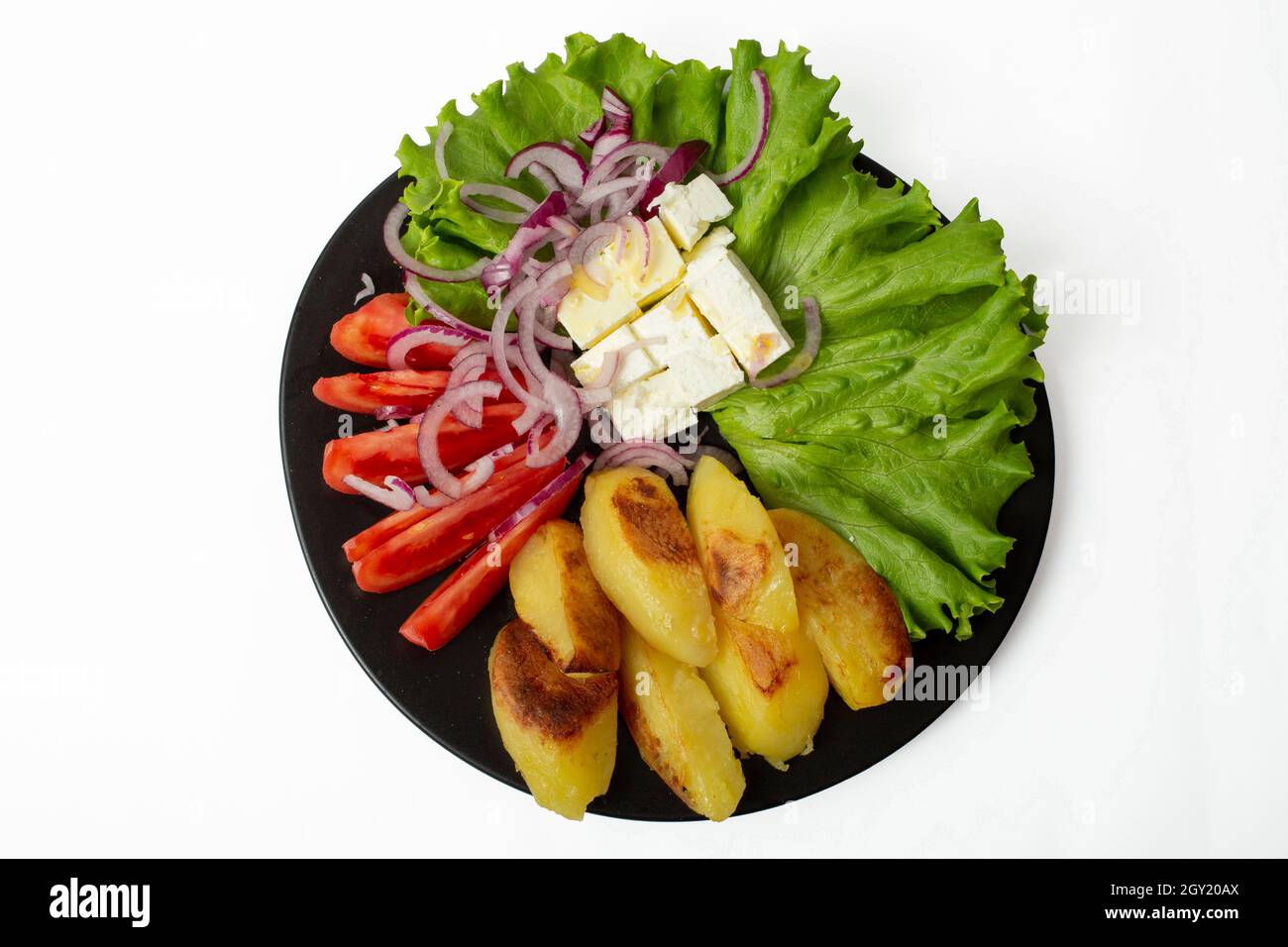 Black plate full of baked potatoes, cottage cheese, sliced tomatoes, sliced red onion, a lettuce leaf and olive oil. Mediterranean food isolated on wh Stock Photo