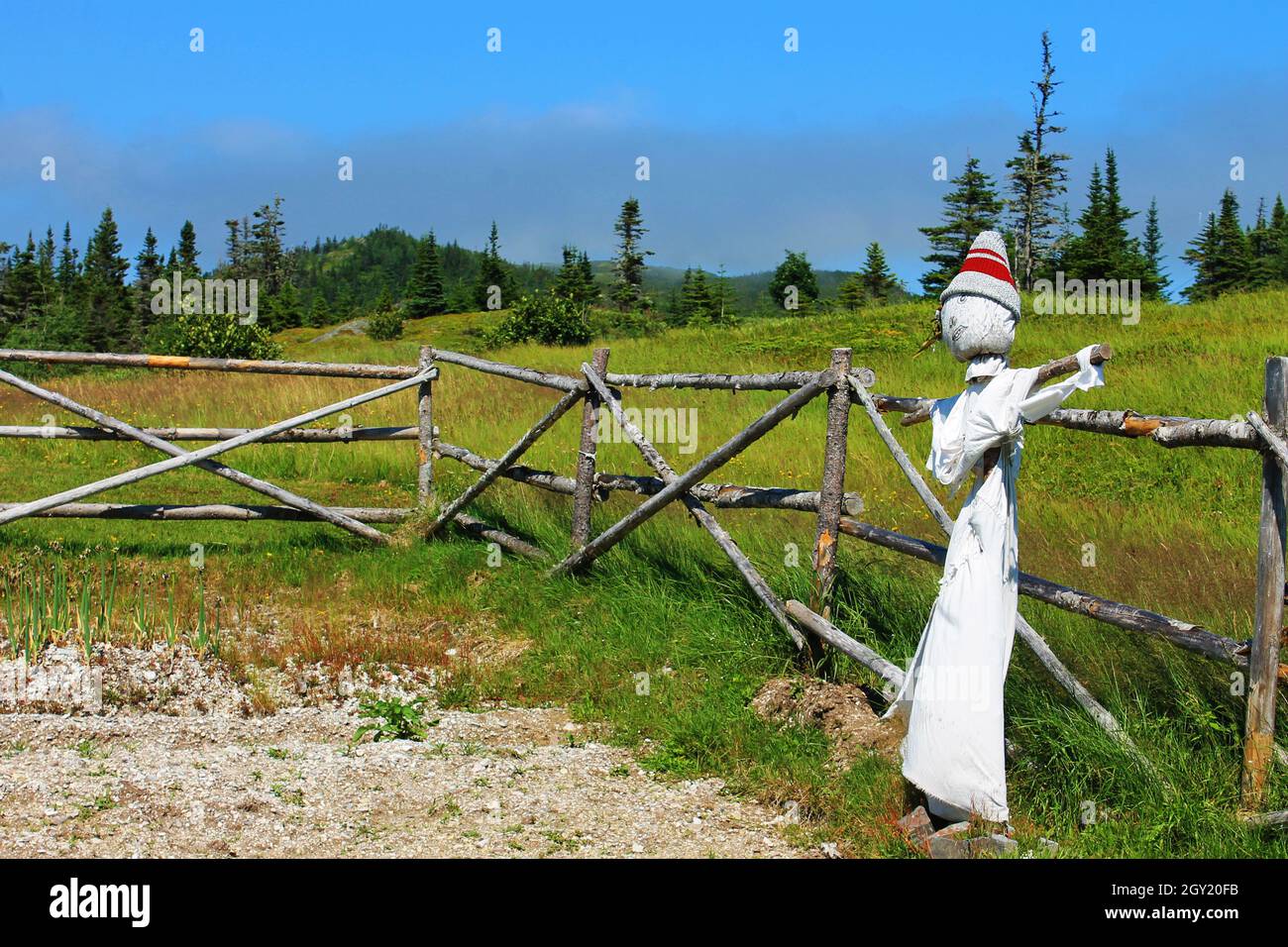 A scarecrow in a small vegetable garden enclosed by a rustic log fence, Random Passage site, New Bonaventure, Newfoundland Labrador. Stock Photo
