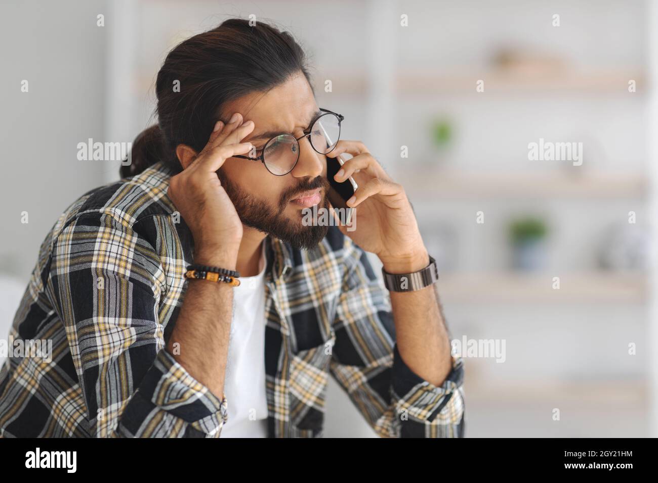 Upset middle-eastern guy having phone conversation, home interior Stock Photo