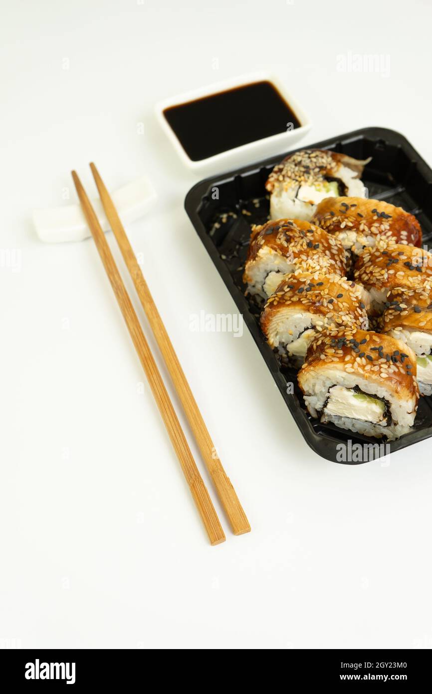 Sushi delivery box on a white background. Japanese menu in black transport box with chopsticks Stock Photo