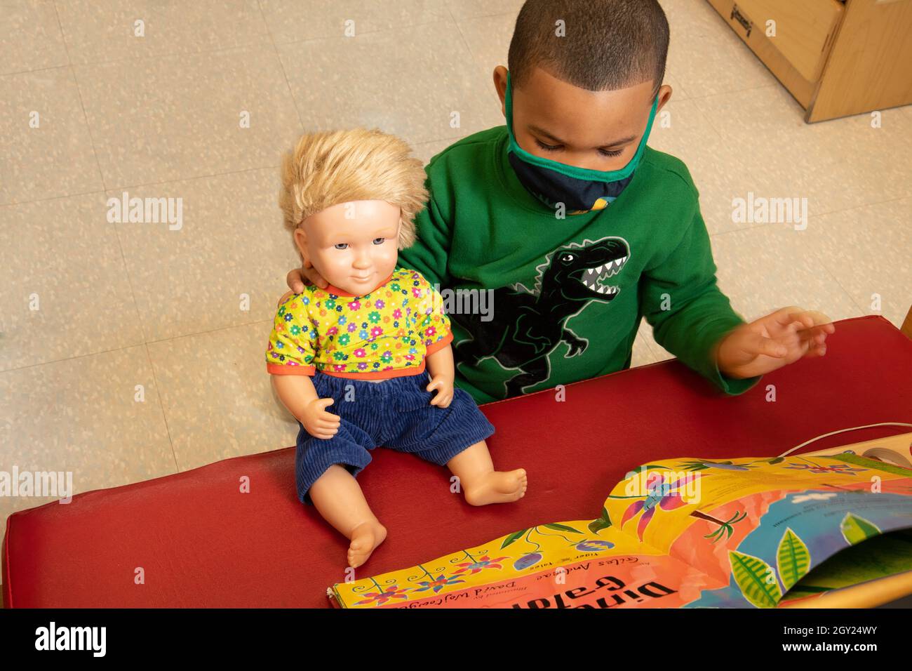 Education Preschool 3-4 year olds boy playingin family area, reading book to doll, book placed so doll can see it Stock Photo