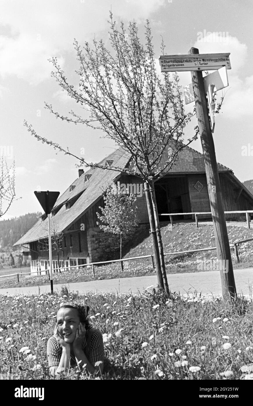 Eine junge Frau auf einer Wiese vor einem alten Haus im Schwarzwald, Deutschland 1930er Jahre. A young woman lying on a meadow in front of an old house in the Black Forest, Germany 1930s. Stock Photo