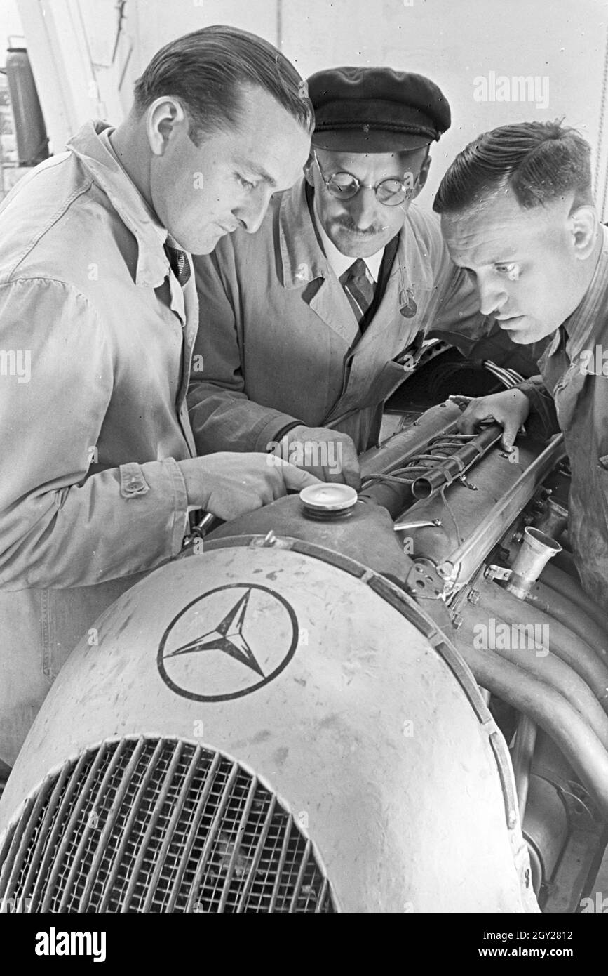 Der Autorennfahrer Hermann Lang in der Autowerkstatt im Gespräch mit Automechanikern, Deutschland 1930er Jahre. The racing driver Hermann Lang talking to car mechanics in the autoshop, Germany 1930s. Stock Photo