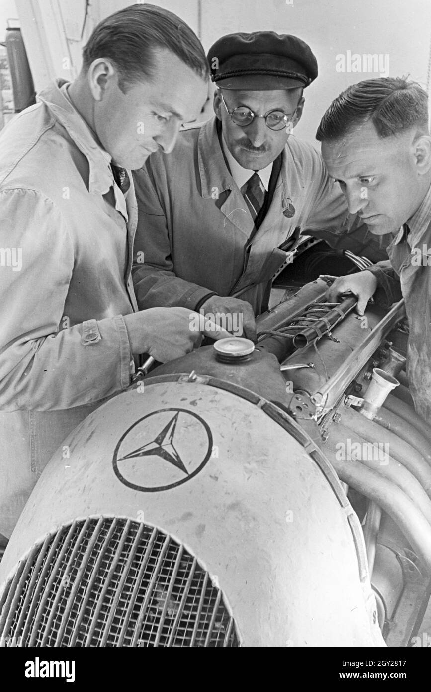 Der Autorennfahrer Hermann Lang in der Autowerkstatt im Gespräch mit Automechanikern, Deutschland 1930er Jahre. The racing driver Hermann Lang talking to car mechanics in the autoshop, Germany 1930s. Stock Photo