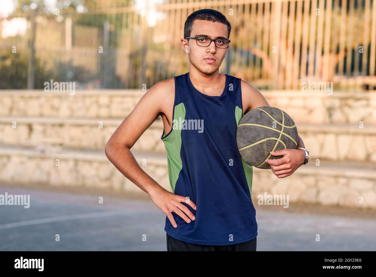 Young child holding a basketball. Serious teenager with basket ball on basketball court at sunset. Stock Photo