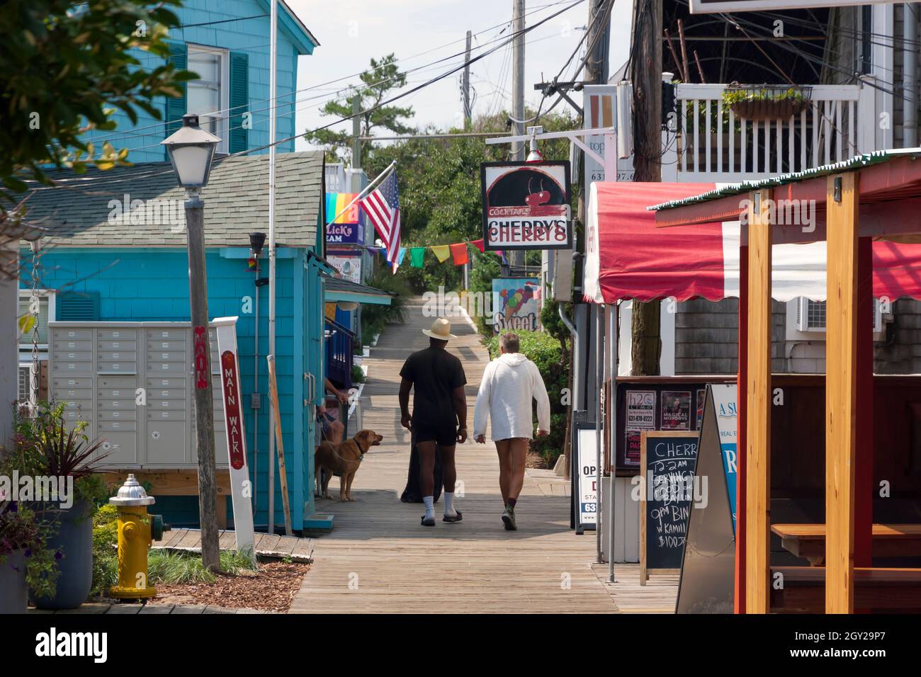 Gay couple walking along the boardwalk through the central business district (Town) of Cherry Grove on Fire Island, New York, Suffolk County, USA. Stock Photo