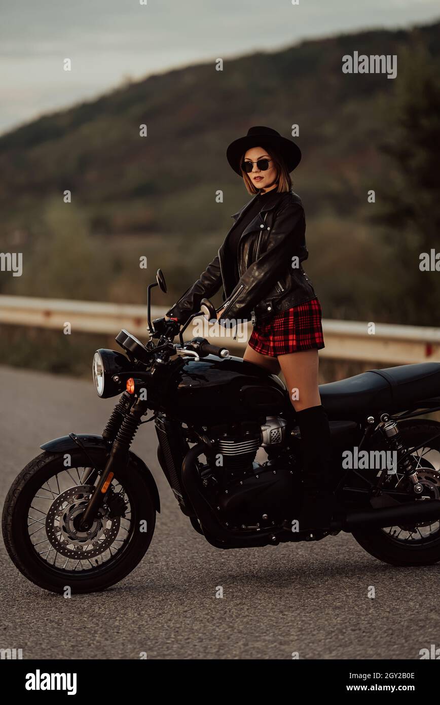 Stylish motorcyclist woman in mini skirt, leather jacket stands on
