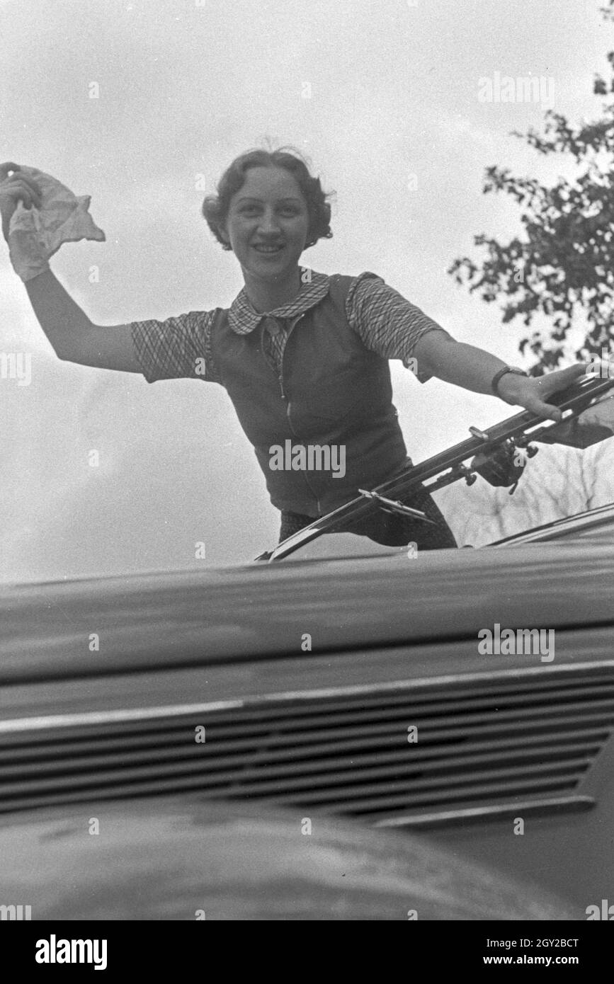 Eine junge Frau reinigt die Windschutzscheibe an ihrem Cabrio, Deutschland 1930er Jahre. A young woman cleaning the windscreen of her convertible, Germany 1930s. Stock Photo