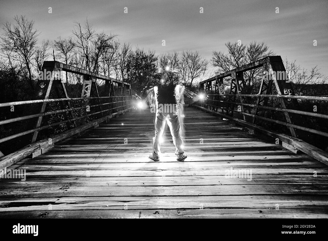 Glowing man phasing in and out of invisibility on a metal bridge in black and white Stock Photo
