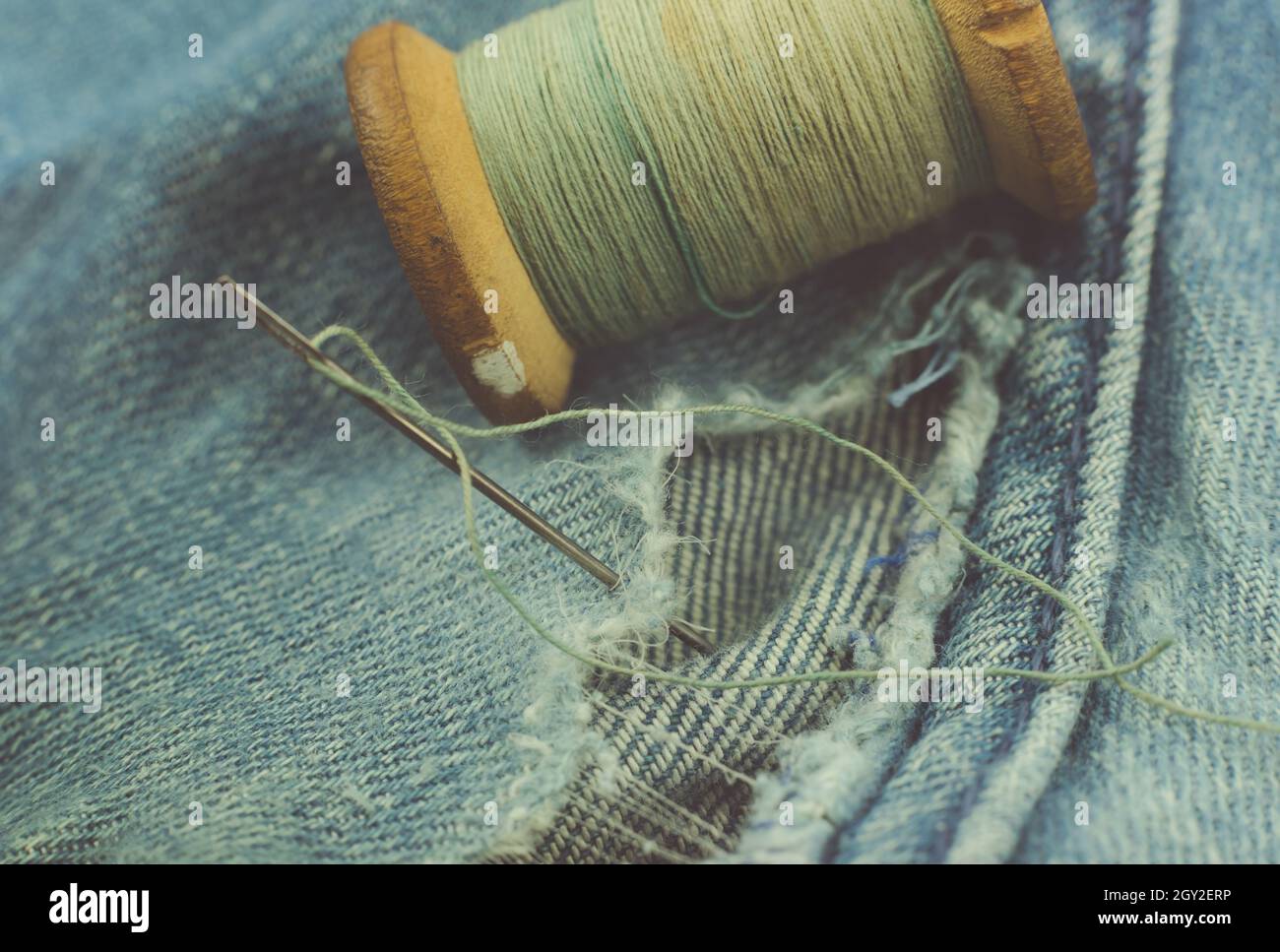 Hole in jeans. Retro thread with a needle to sew up torn jeans Stock