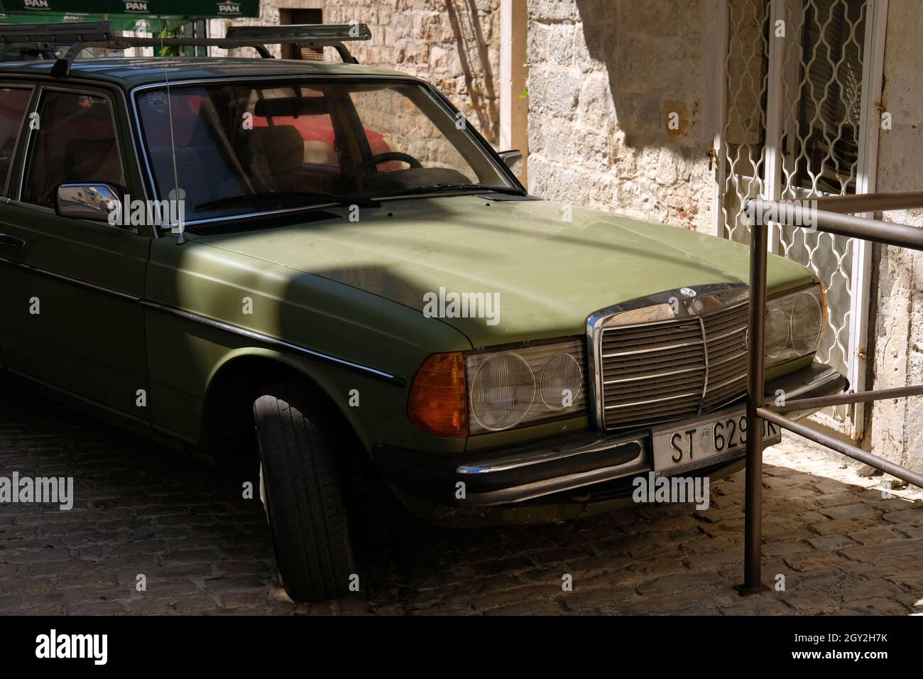 Kastela, Croatia. August 17 2021. Classic green Mercedes Benz 1W123 parked in the narrow street of the old town Stock Photo