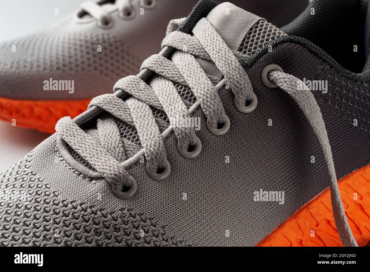 Lacing up the sneakers. Elastic laces of gray mesh fabric sneakers with orange grooved sole. Modern textile trainers for sport and active lifestyle. Stock Photo