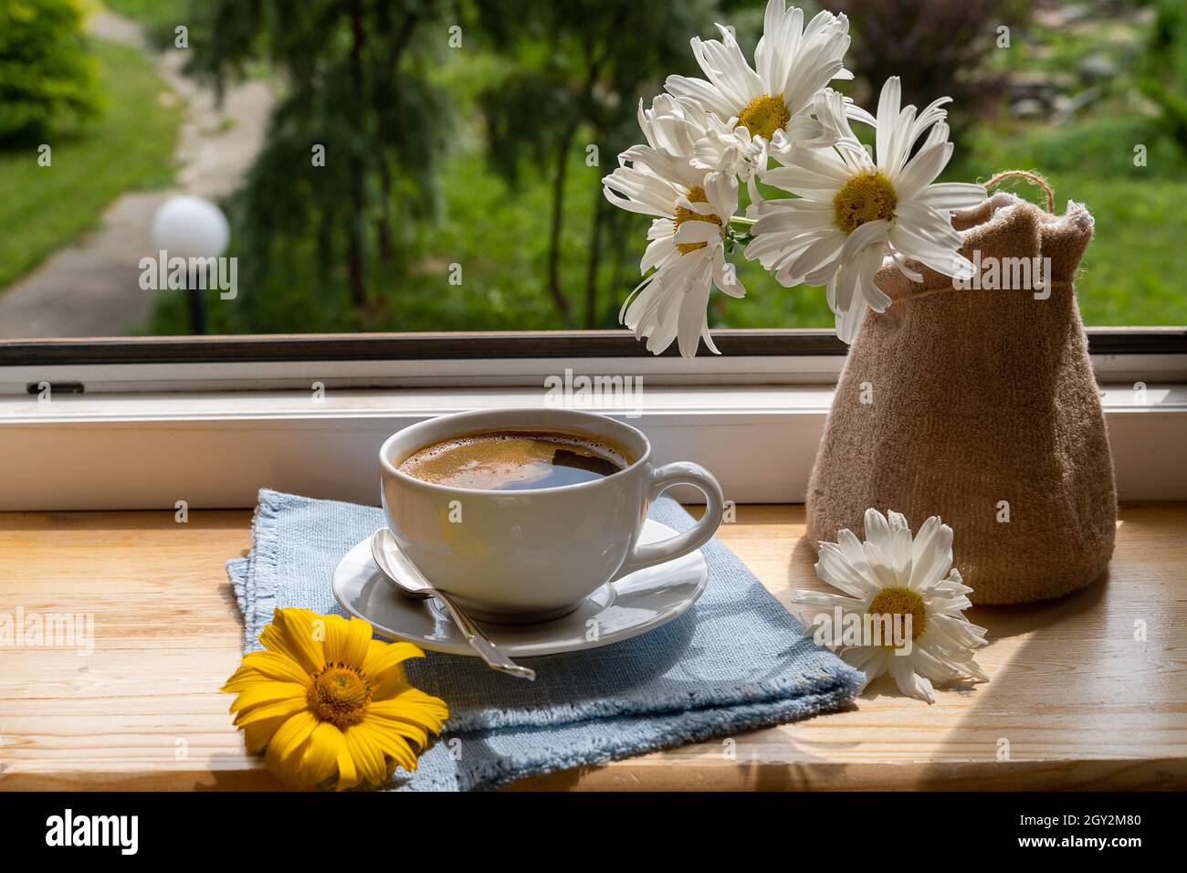 A cup of black coffee and garden flowers on the windowsill under the rays  of the sun, next to beautiful flowers, vertical shot Stock Photo - Alamy