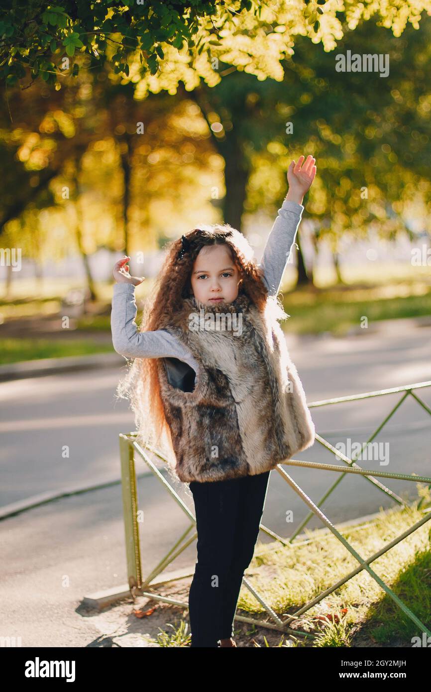 Stylish baby girl 45 year old wearing boots, fur coat standing in park