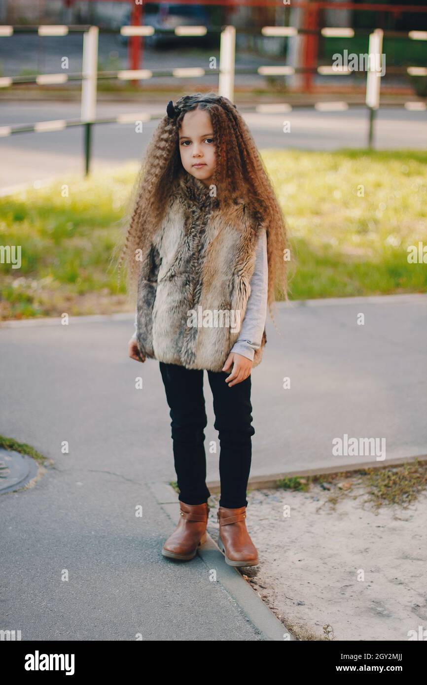Stylish baby girl 4-5 year old wearing boots, fur coat, moving and playing. Autumn fall season Stock Photo