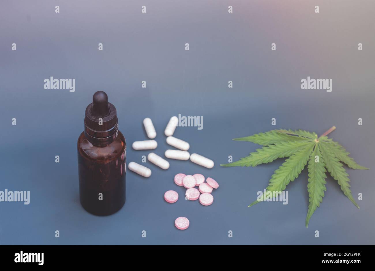 CBD pills. Group of CBD capsules and pink cannabidiol pills and hemp leaves on blue background. Assorted medical cannabis products. Medical marijuana Stock Photo