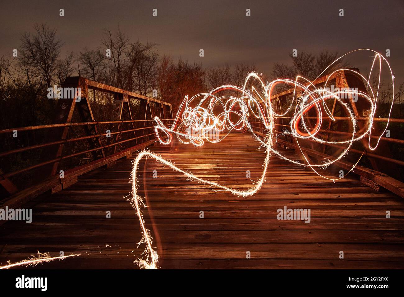 Lassoes and ropes of warm white light intertwine across a metal bridge at dusk Stock Photo