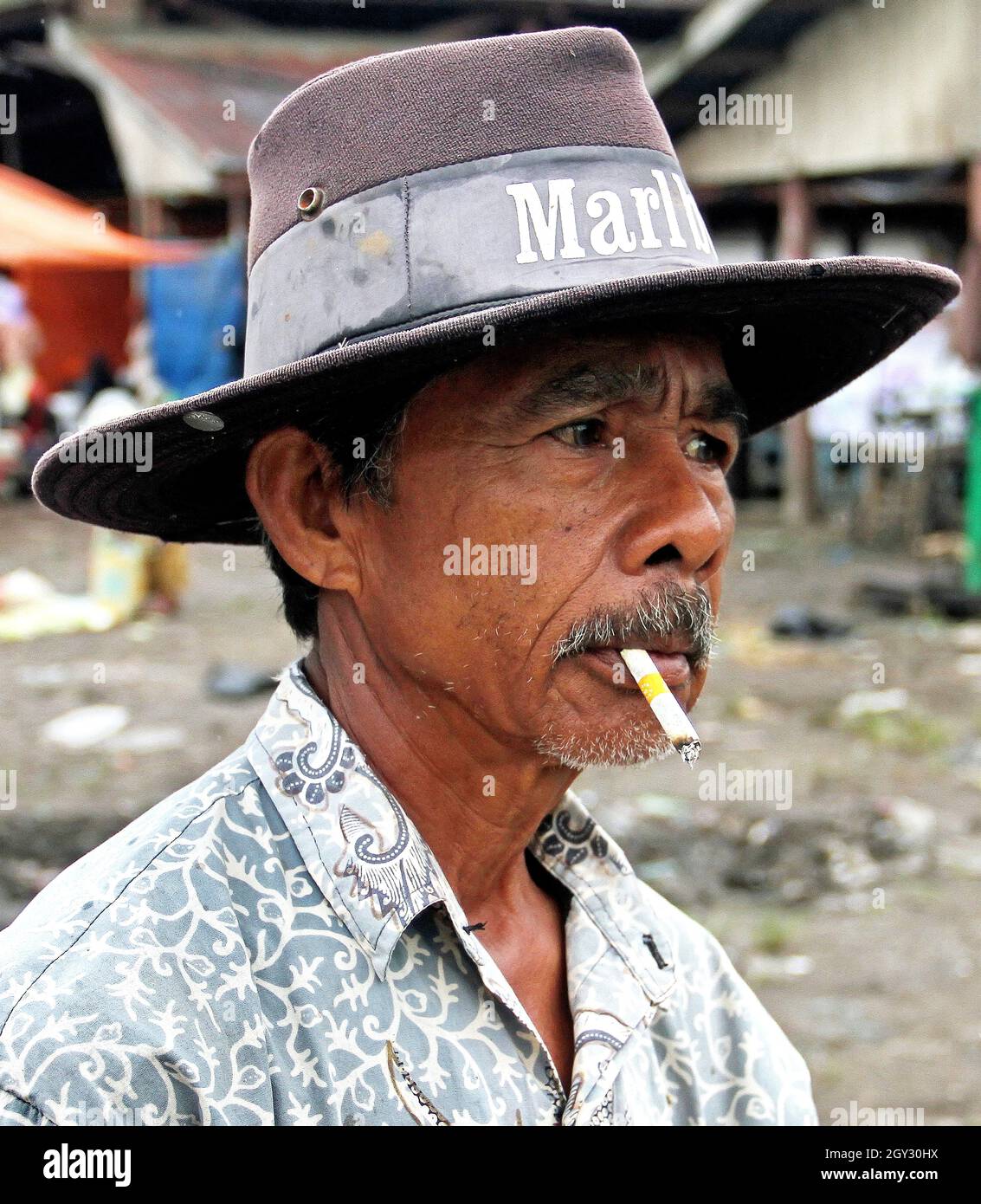 A Indonesian man wearing a Marlboro cowboy hat and smoking a cigarette. This was taken in an outdoor market in Bukittinggi, West Sumatra, Indonesia. Stock Photo