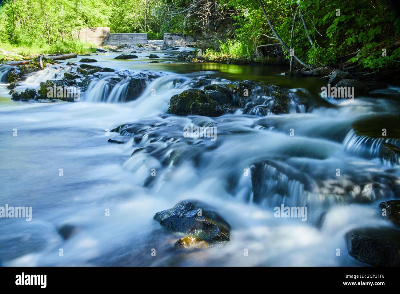 Quaint peaceful smooth waterfalls over rocks with small barrier in background Stock Photo