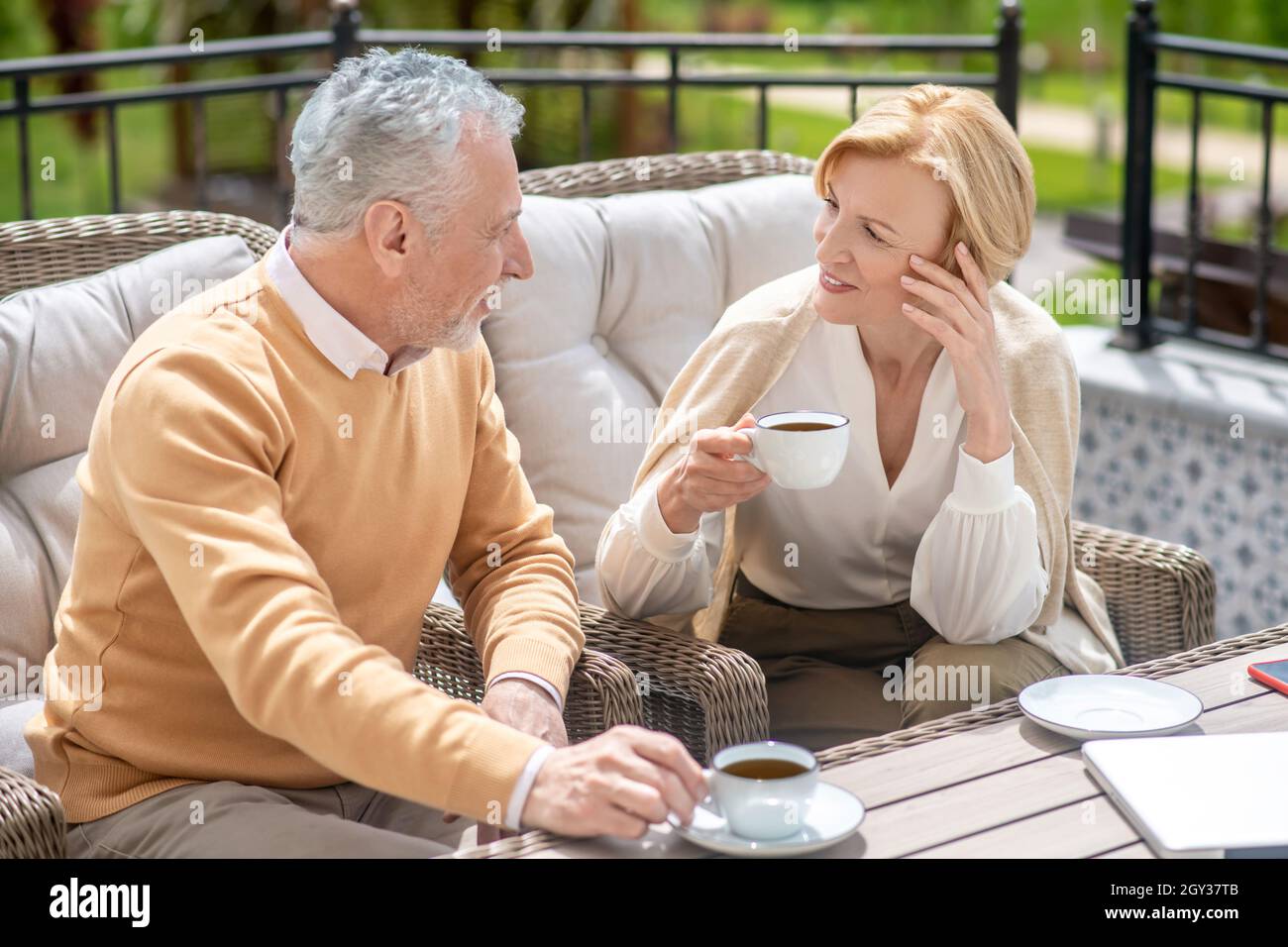 Two middleaged people seated in armchairs talking on the terrace