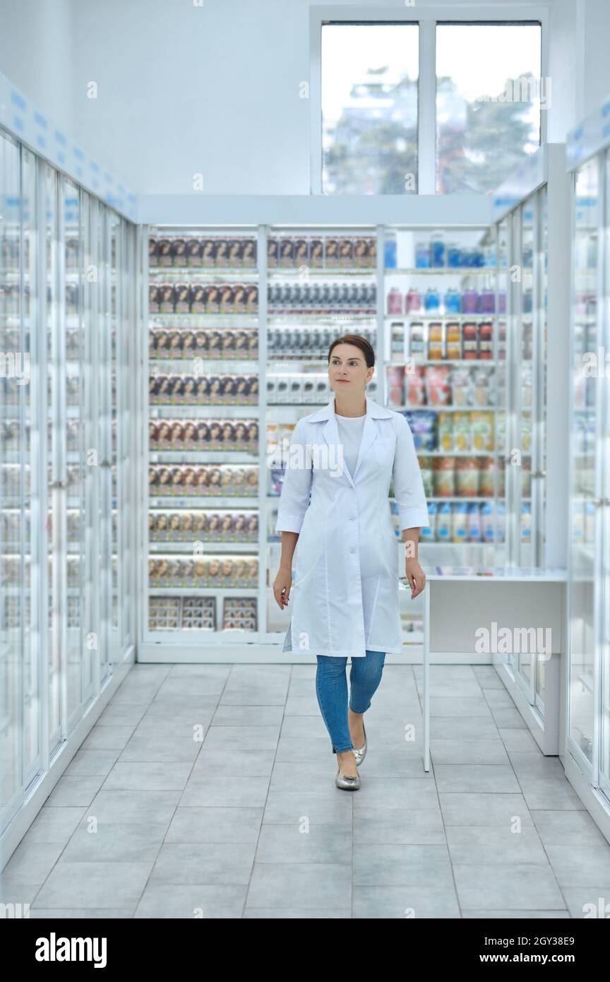 Woman in laboratory coat between shelves with medicines Stock Photo