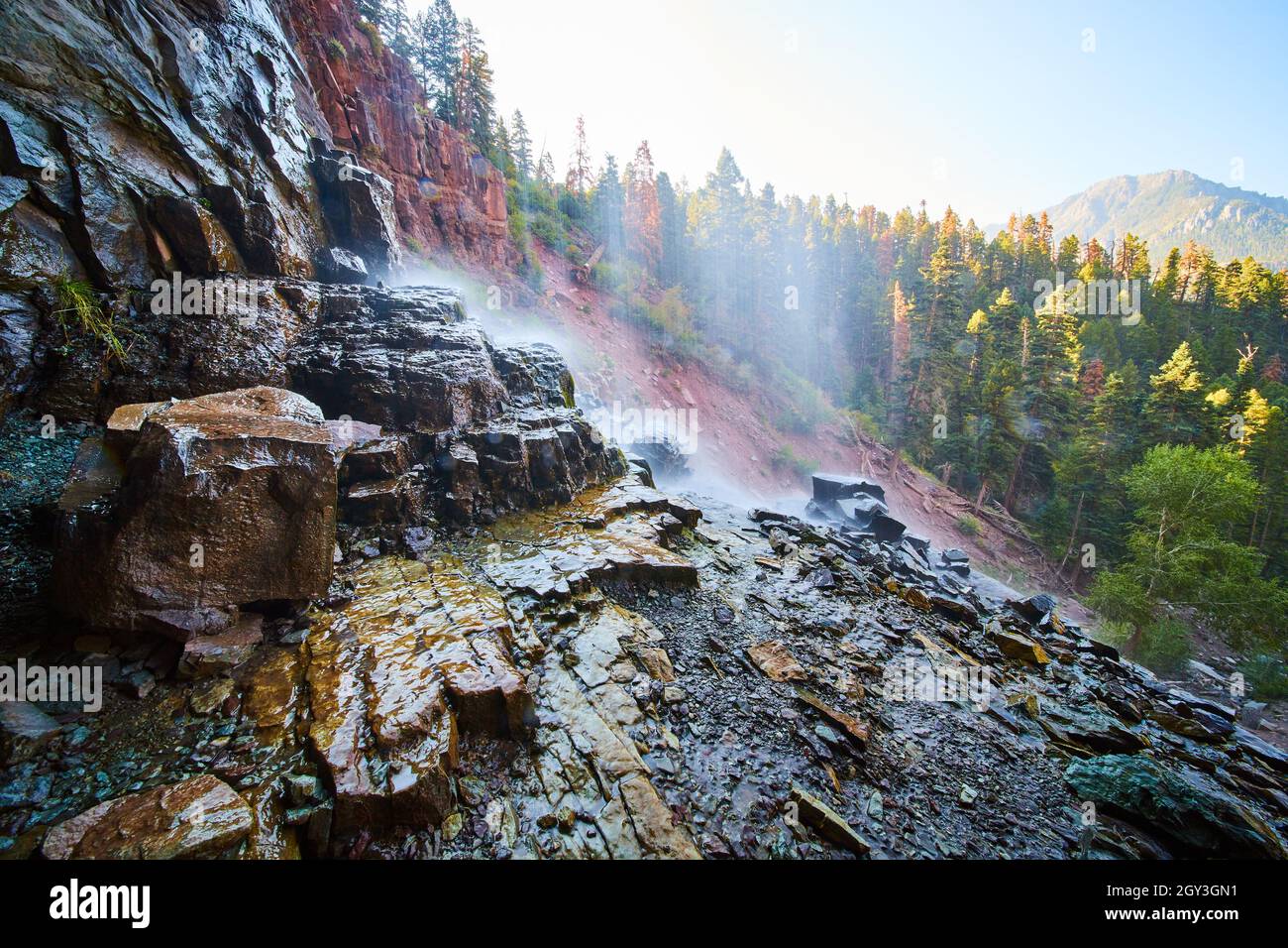 View behind waterfall with wet slippery rocks overlooking mountain in distance Stock Photo