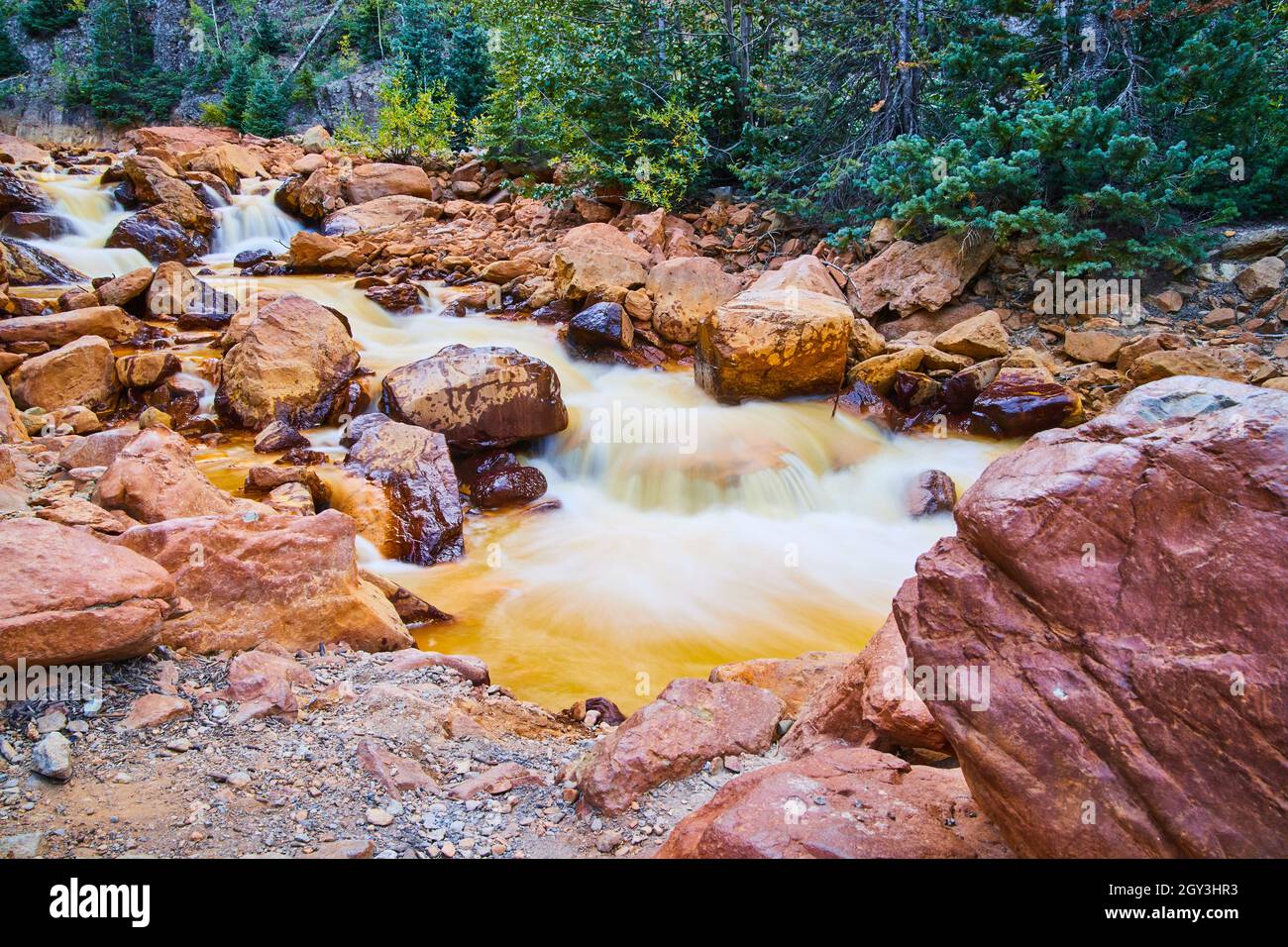 River lined with large red rocks and detail of cascading waterfalls ...