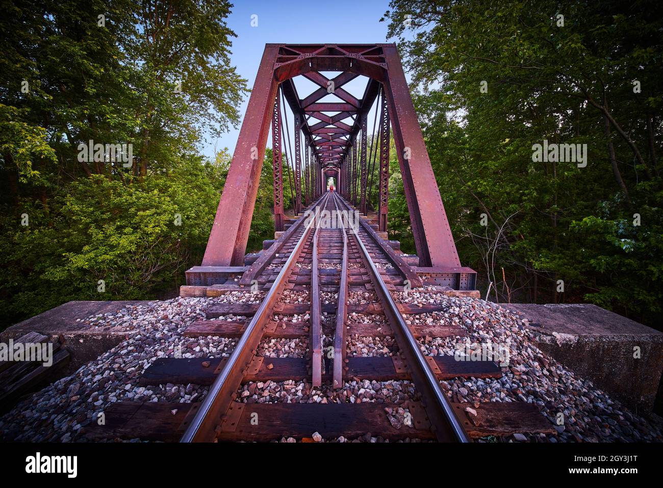 Wide view on train tracks with industrial bridge and train at end approaching Stock Photo