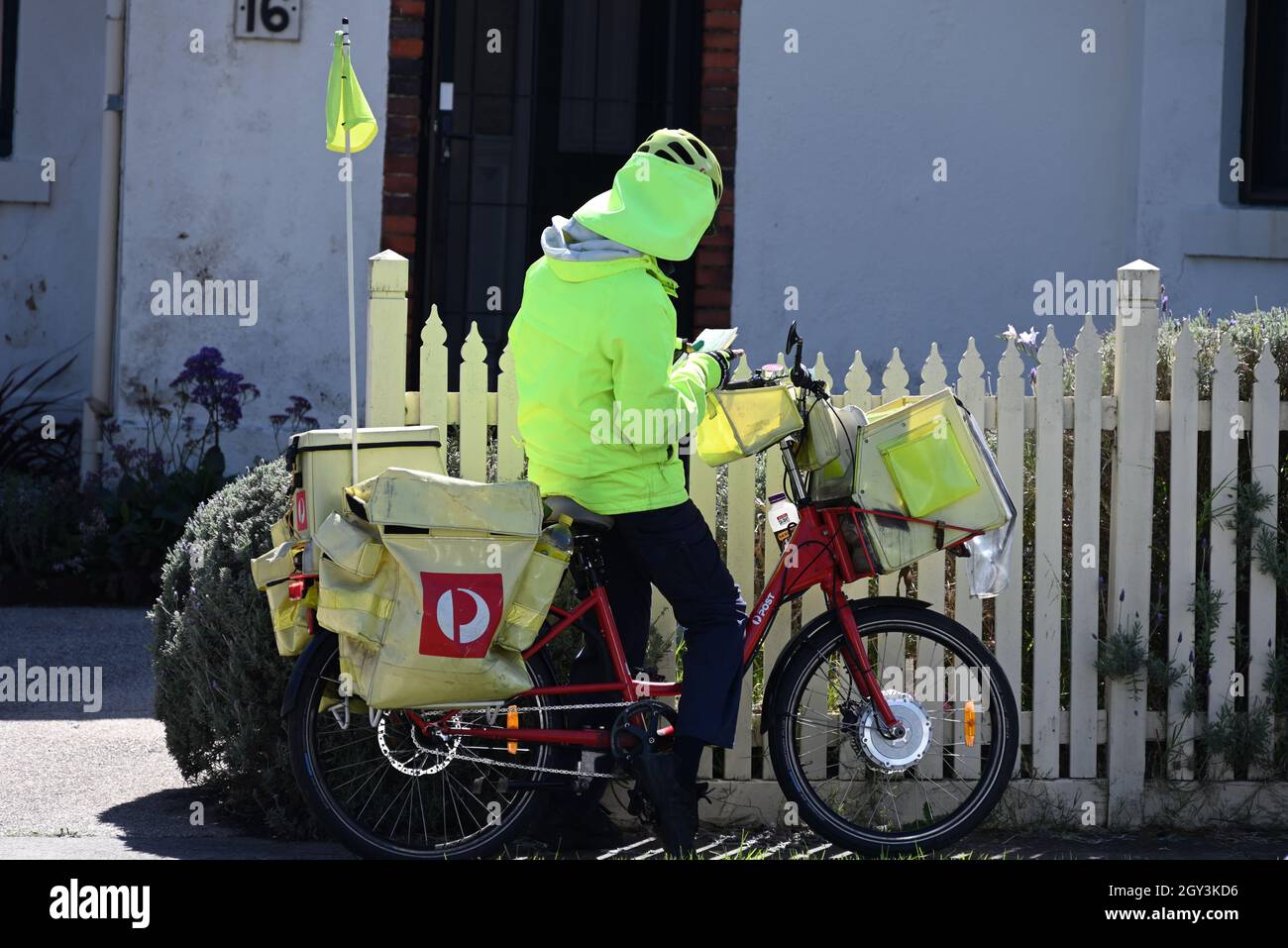 An Australia Post postie on a bike outside a house, in standard fluorescent protective gear, sorting letters. Stock Photo