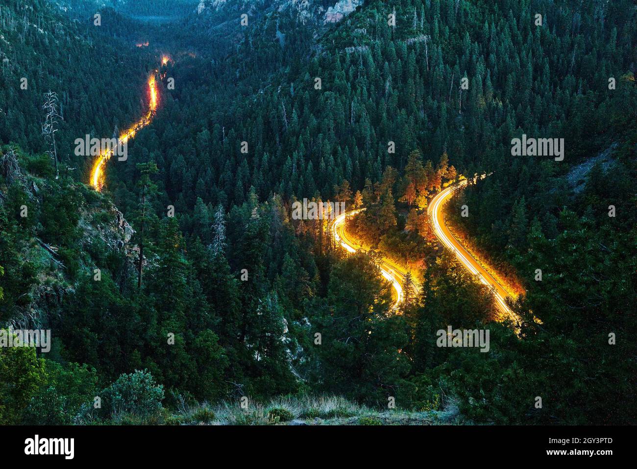 Windy road in mountains with headlights of cars driving through Stock