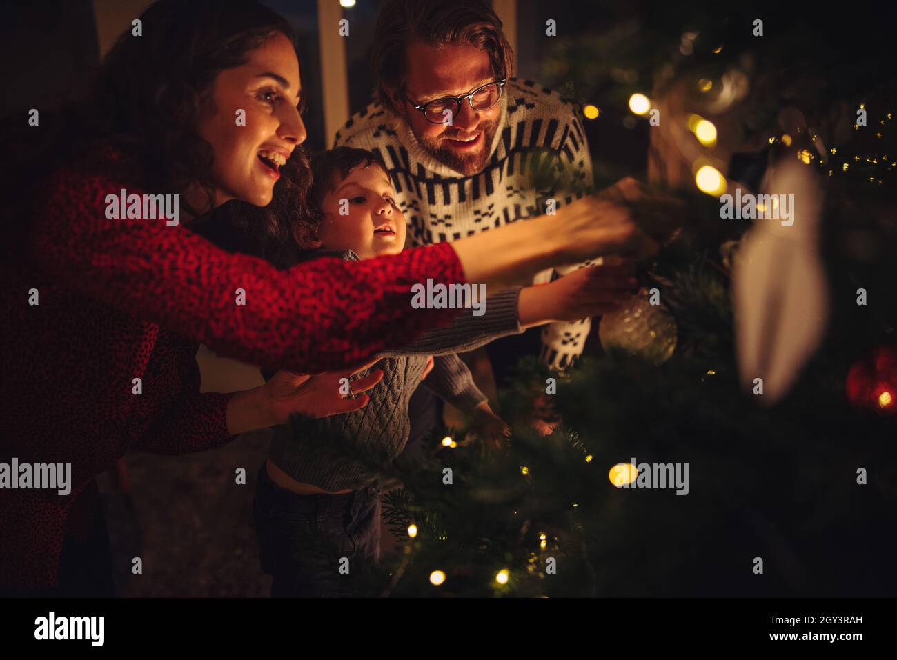 Family of three preparing fir tree for Christmas eve celebrations at home. Family decorating Christmas tree together at home. Stock Photo