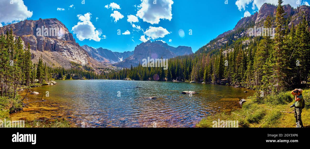Lake in mountains surrounded by pine trees with photographer Stock Photo