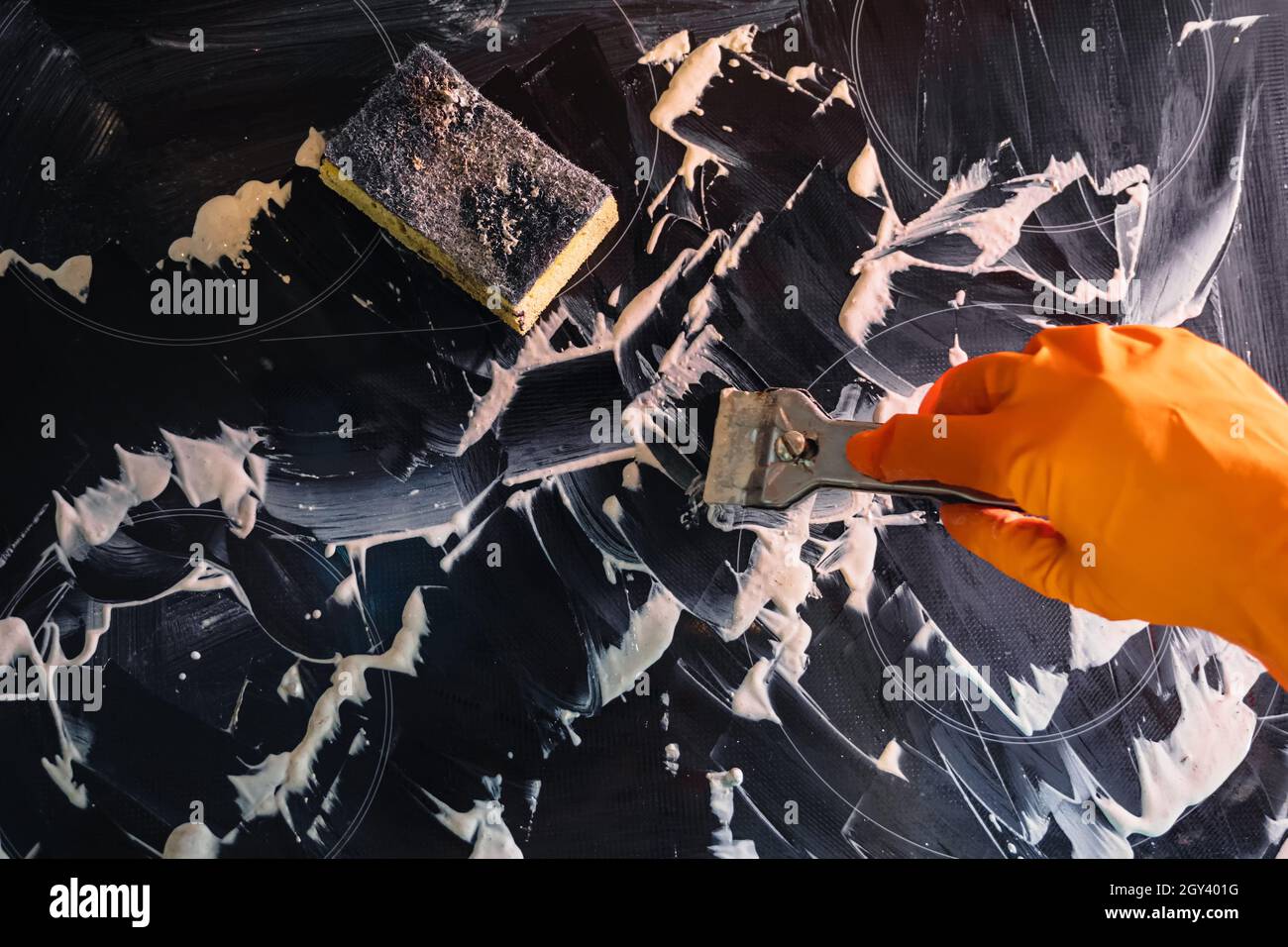 Cooktop with cleaner applied to it. Orange glove, metal scraper and