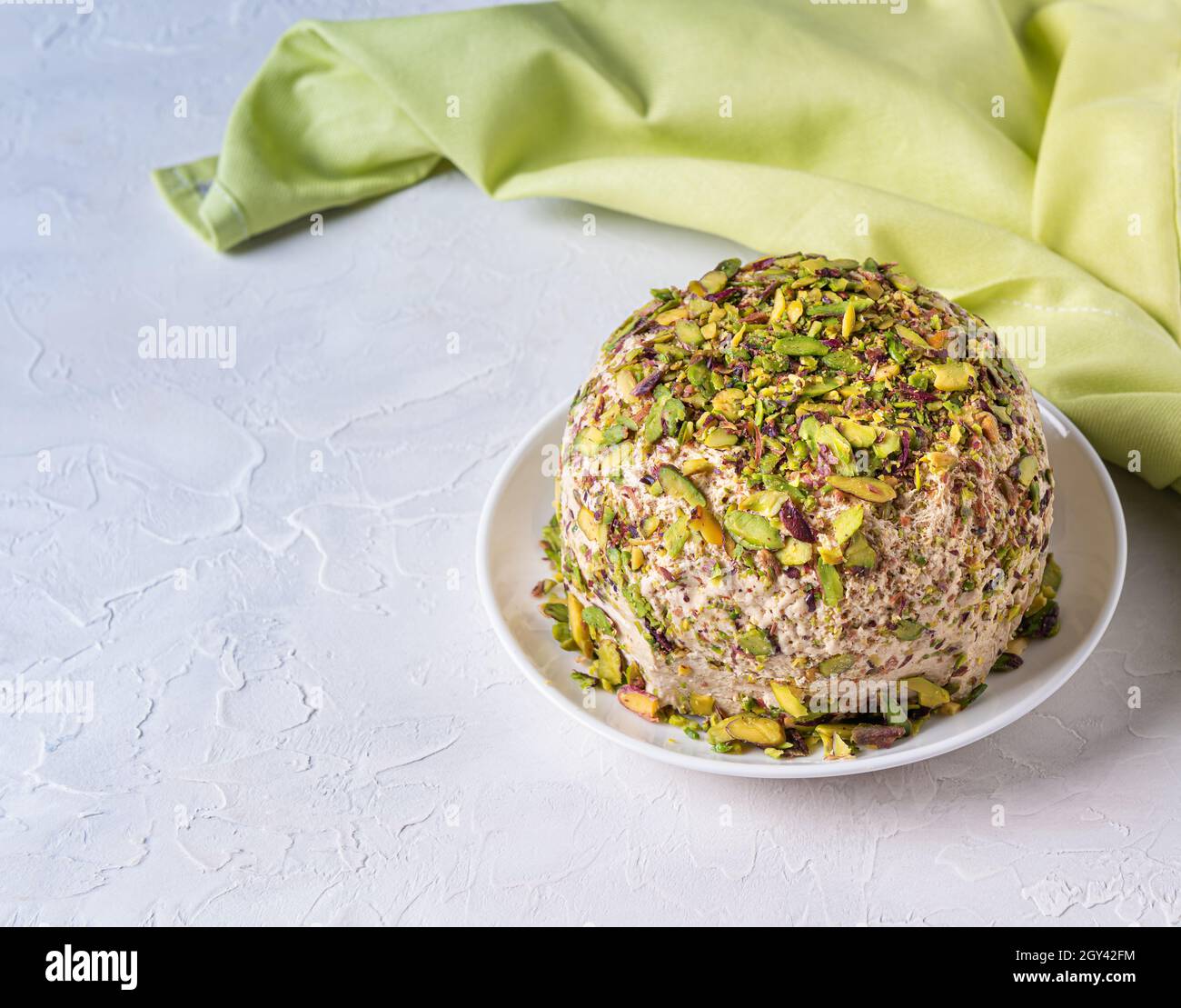 Sesame halva with pistachios nuts on white background with green linen napkin on side and copy space. Turkish delight. Traditional middle eastern swee Stock Photo
