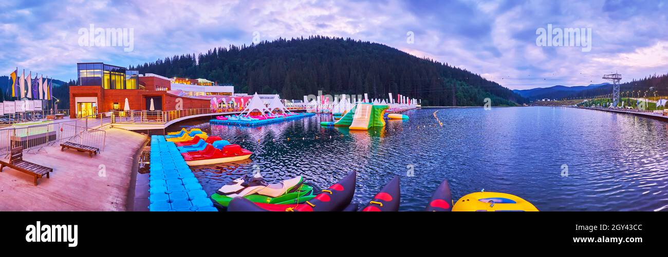The pleasant evening walk around the picturesque mountain Molodist (Youth) Lake, with tourist boats and water park, Bukovel, Carpathians, Ukraine Stock Photo