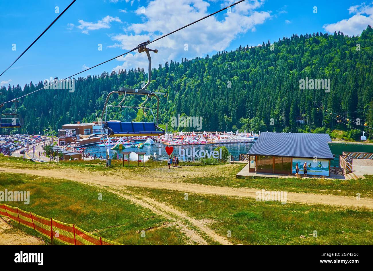 BUKOVEL, UKRAINE - JULY 25, 2021: The mountain Molodist (Youth) Lake with beach, spa club, water attractions and green mountains of Gorgany Range in t Stock Photo