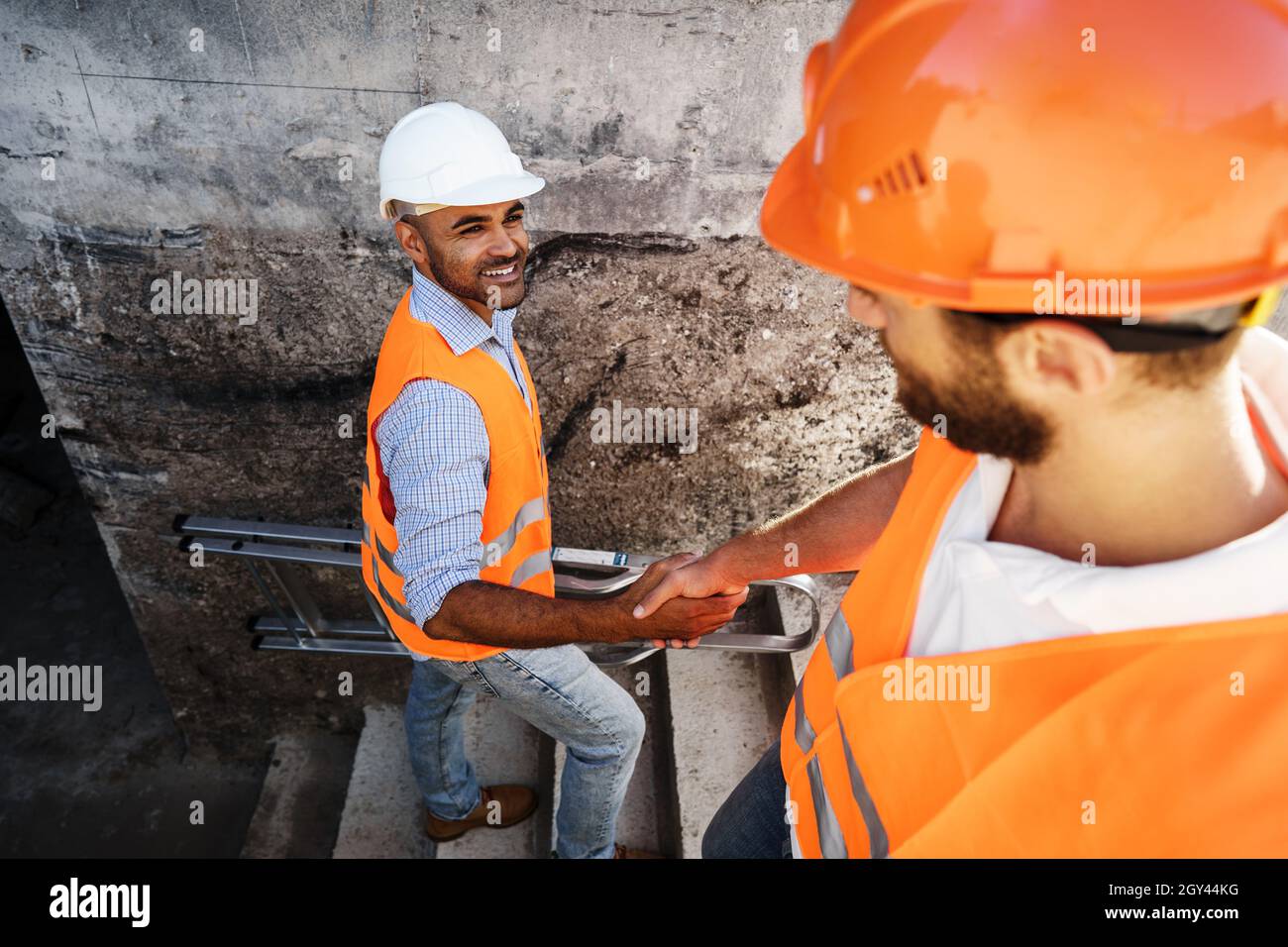 Two men engineers in workwear shaking hands against construction site. Stock Photo