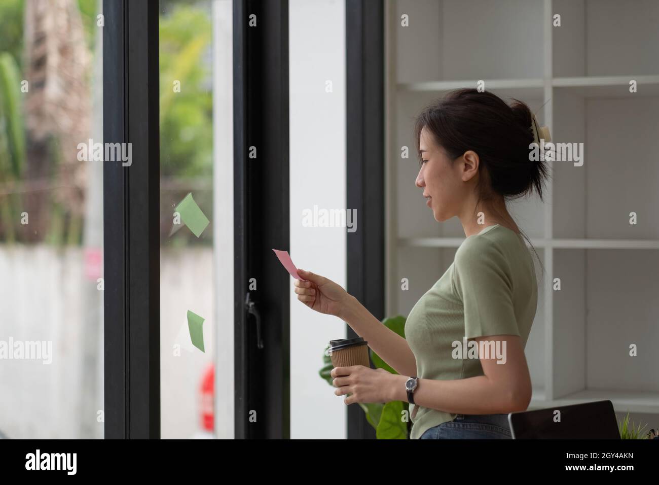 Creative business asian woman reading sticky notes on glass wall at office. Stock Photo