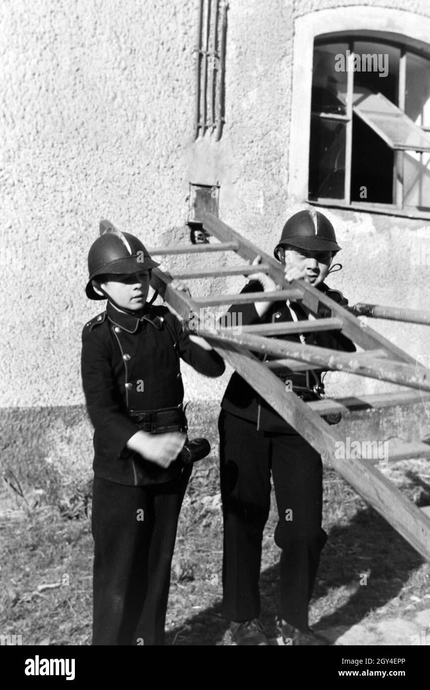 Zwei uniformierte Jungen von der Kinderfeuerwehr halten die Leiter bei einer Feuerwehrübung, Deutschland 1930er Jahre. Two uniformed boys of the junior firefighters are holding a ladder during a firefighter training, Germany 1930s. Stock Photo