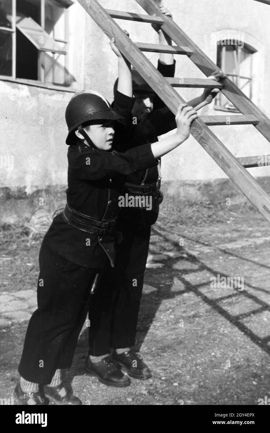 Zwei uniformierte Jungen von der Kinderfeuerwehr halten die Leiter bei einer Feuerwehrübung, Deutschland 1930er Jahre. Two uniformed boys of the junior firefighters are holding a ladder during a firefighter training, Germany 1930s. Stock Photo