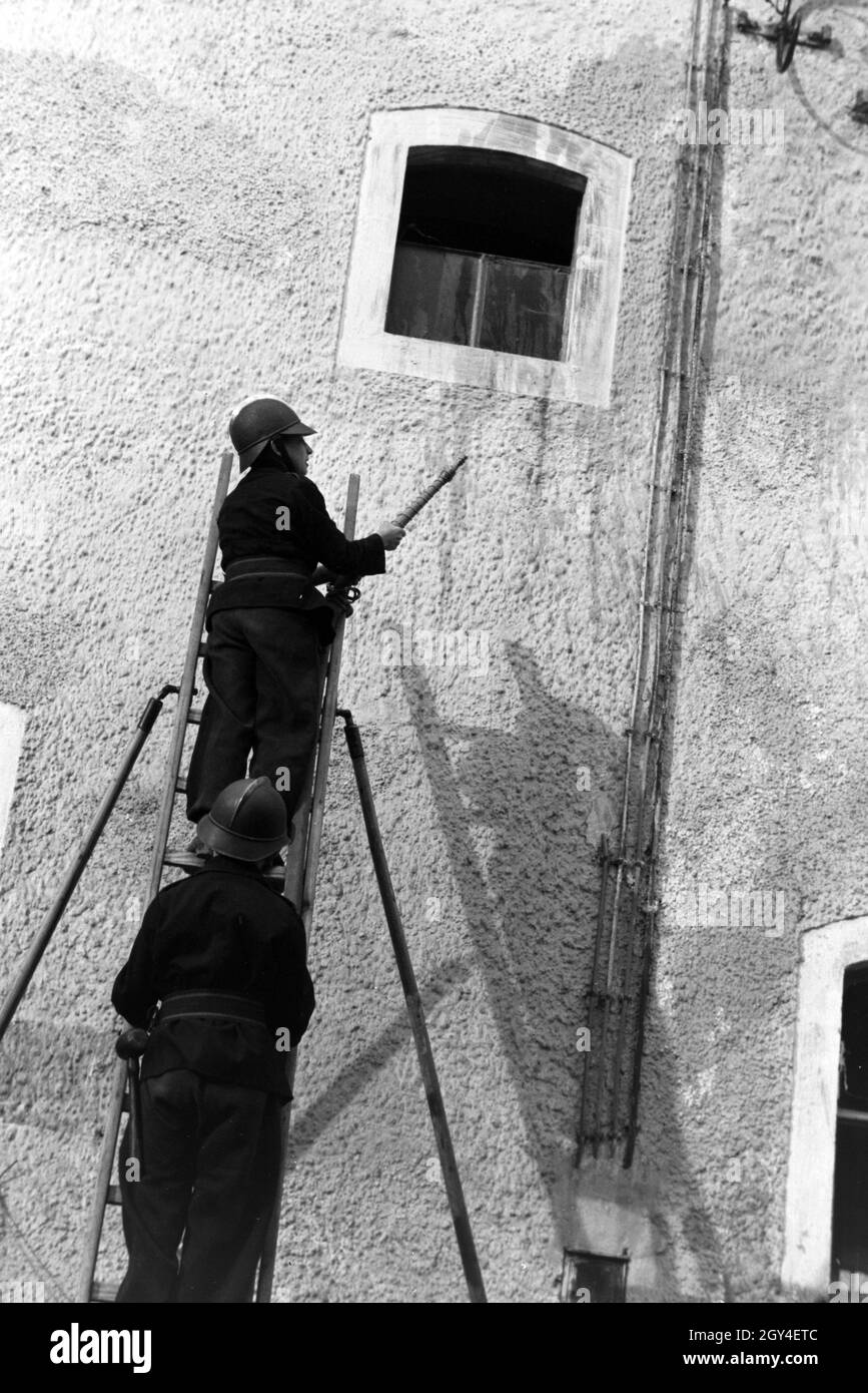 Zwei Jungen von der Kinderfeuerwehr bei einer Feuerwehrübung mit dem Löschschlauch auf einer Leiter, Deutschland 1930er Jahre. Two boys of the junior firefighters standing on a ladder with the water hose during a firefighter training, Germany 1930s. Stock Photo