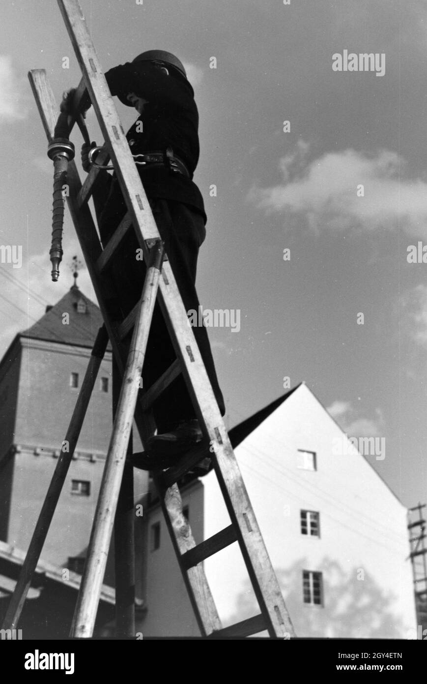 Ein Junge von der Kinderfeuerwehr bei einer Feuerwehrübung mit dem Löschschlauch auf einer Leiter, Deutschland 1930er Jahre. A boy of the junior firefighters standing on a ladder with the water hose during a firefighter training, Germany 1930s. Stock Photo