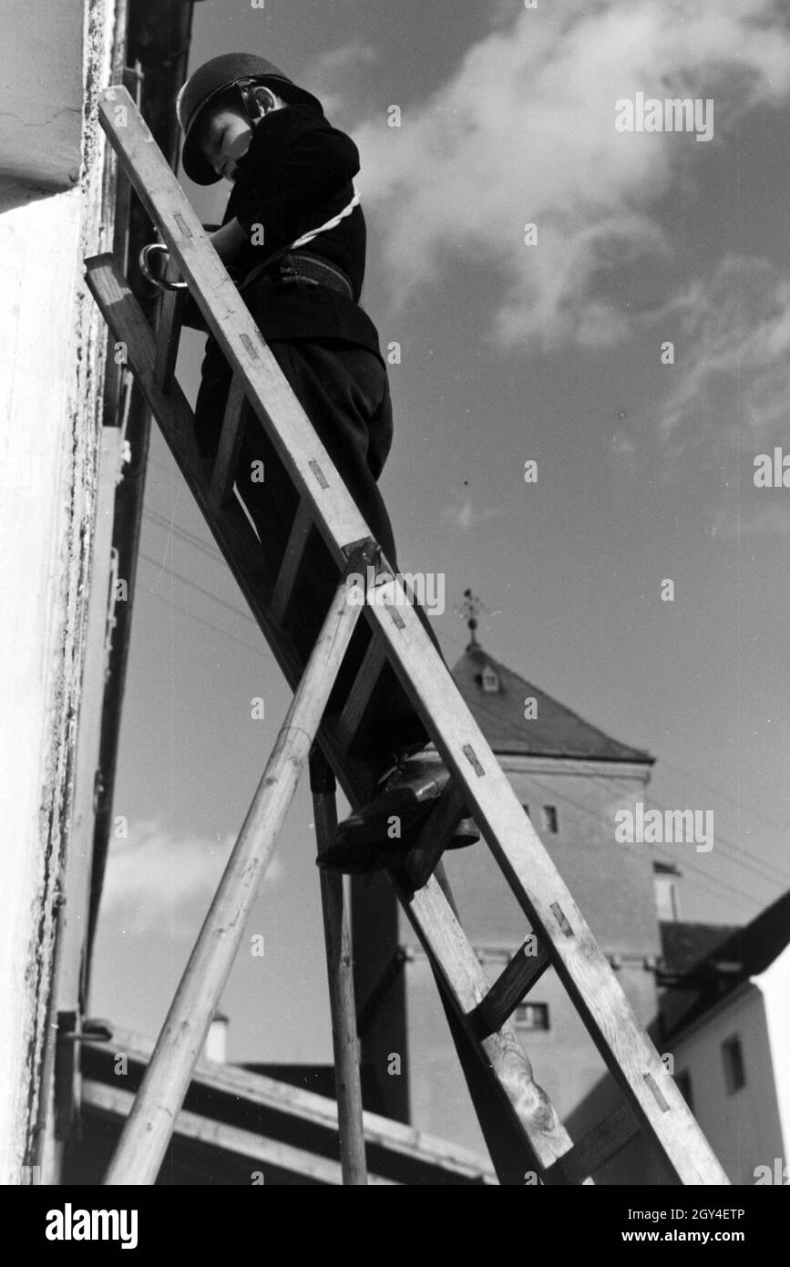 Ein Junge von der Kinderfeuerwehr erklettert bei einer Feuerwehrübung eine Leiter, Deutschland 1930er Jahre. A boy of the junior firefighters is climbing up a ladder during a firefighter training, Germany 1930s. Stock Photo