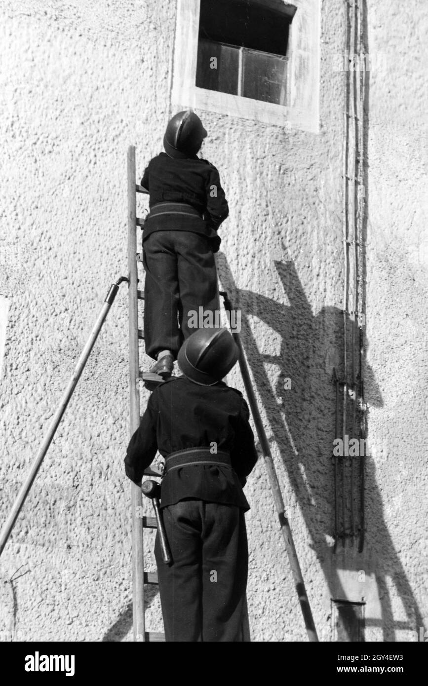 Zwei Jungen von der Kinderfeuerwehr bei einer Feuerwehrübung mit dem Löschschlauch auf einer Leiter, Deutschland 1930er Jahre. Two boys of the junior firefighters standing on a ladder with the water hose during a firefighter training, Germany 1930s. Stock Photo